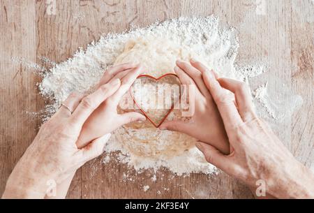 .Hände, Backen und Herz Formen sich mit einem Mädchen und Großmutter lernen, wie man in der Küche ihres Hauses zusammen backen. Familie, Kinder und Essen mit Stockfoto