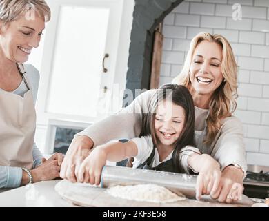.Mutter, Großmutter und Kind kochen und backen mit Nudelholz für Gebäck, Kuchen oder Pizza zusammen in der Familienküche. Frau, Senioren und Mädchen helfen Stockfoto