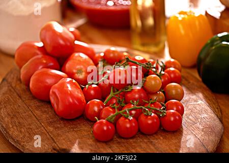 Verlockende Tomaten. Eine Pflaume und Kirschtomaten auf einem Tisch in einer Küche. Stockfoto