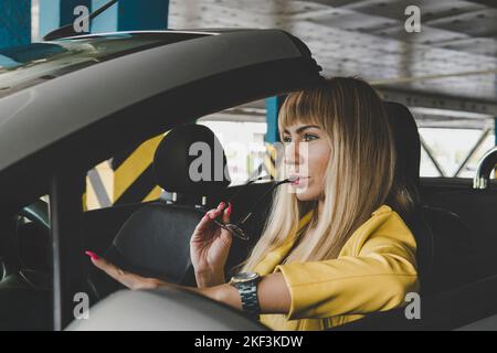 Porträt junge Dame träumen, während sich an der Tür des Automobils. Sie lokalisiert innen davon. Modische Frau beißt ihre Brille mit einem nachdenklichen Ex Stockfoto