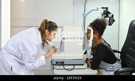 Augenärztin testet das Sehvermögen eines Mädchens mit speziellen optischen Apparaten in der Klinik Stockfoto