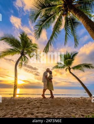 Paar Männer und Frauen beobachten den Sonnenuntergang am Strand, Bang Tao Beach während des Sonnenuntergangs in Phuket Thailand und Palmen während des Sonnenuntergangs am Strand. Stockfoto