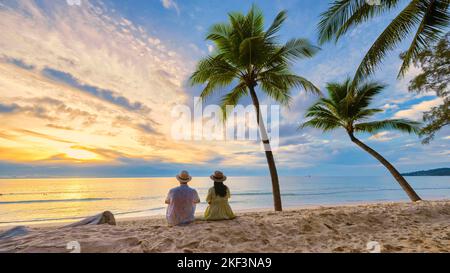 Paar Männer und Frauen beobachten den Sonnenuntergang am Strand, Bang Tao Beach während des Sonnenuntergangs in Phuket Thailand und Palmen während des Sonnenuntergangs am Strand. Stockfoto