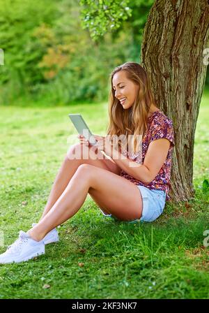 Ihre Freizeit verbringt sie an der frischen Luft. Eine junge Frau benutzt ein digitales Tablet im Park. Stockfoto