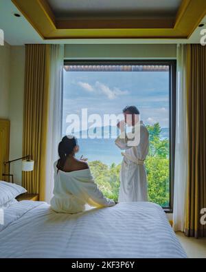 Ein paar Männer und Frauen wachen im Hotelzimmer mit Kaffee auf und blicken auf das Meer. Stockfoto