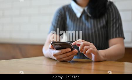 Hübsche junge asiatische Frau, die im Café chillt, ihr Smartphone benutzt und ihren Freunden SMS schreibt Stockfoto