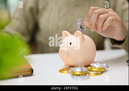 Nahaufnahme, Eine weibliche Münze in ein Sparschwein. Geld sparen und finanzielles Anlagekonzept Stockfoto