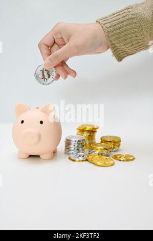 Eine weibliche Hand legen Münze in ein Sparschwein, Stapel von goldenen und silbernen Münzen auf weißem Hintergrund. Sparkonzept Stockfoto