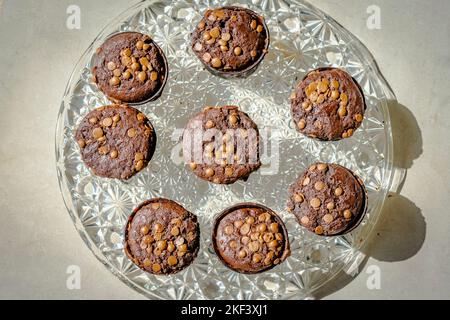 Blick von oben auf hausgemachte Muffins mit Schokoladenkuchen auf einer Glasplatte. Direkt über der Nahaufnahme Makrofotografie mit seitlicher Sonneneinstrahlung. Stockfoto