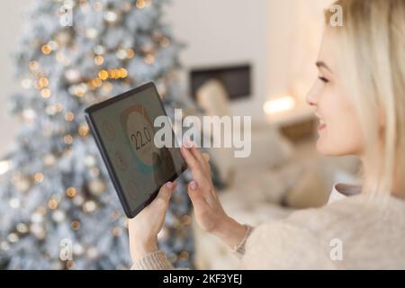 Junge Frau verwendet Anwendung in seinem Smart Home zu Weihnachten Stockfoto