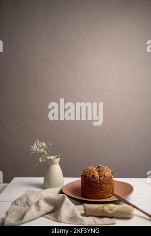 Eine vertikale Aufnahme eines Laibs Brot, das auf einem braunen Teller in der Nähe einer weißen Vase in einem Studio platziert wurde Stockfoto