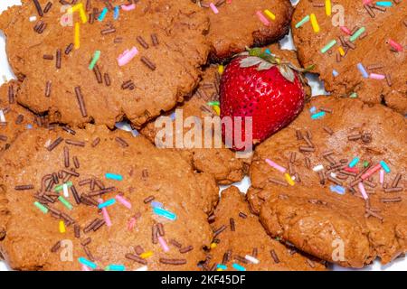 Makrofotografie-Nahaufnahme von hausgemachten Schokoladenkeksen mit farbigen Chips und einer Erdbeere. Direkt über der Makroansicht. Stockfoto