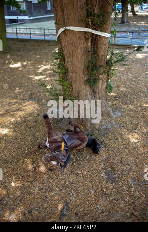 Weißes Band, das um einen Baum gebunden ist, der aufgrund der Infill-Entwicklung mit einem zerbrochenen Spielzeugpferd, das auf dem Gras abgelegt wird, abgeschlagen wird Stockfoto