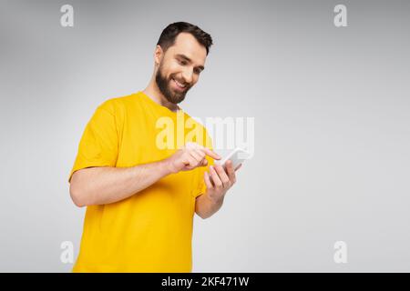 Low-Angle-Ansicht von brünetten bärtigen Mann zeigt auf Mobiltelefon isoliert auf grauem, Stock-Bild Stockfoto