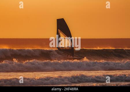 Windsurfer genießt seine letzte Lichtzeit, während er auf einer Welle steht Stockfoto