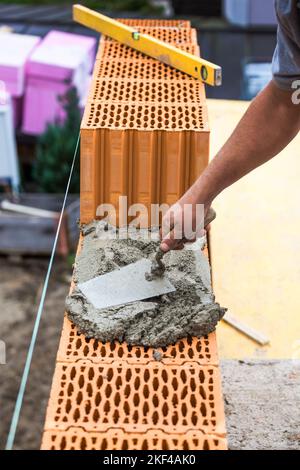 Ein Maurer beim Mauern eines Rohbaues in Massivbauweise. Ziegelmauer eines Einfamilienhauses Stockfoto