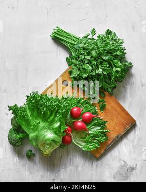 Frischer Radieschen- und Grünsalat aus Eisbergsalat mit Petersilie auf hellem Hintergrund und Holzbrett Stockfoto