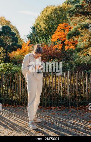 Schöne junge Frau macht Fotos mit einer professionellen Kamera im Herbstwald. Lächelndes Mädchen genießen Herbstwetter. Ruhe, Entspannung, Lifestyle Stockfoto