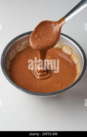Schokolade Karamell-Creme, schlagen mit einem Löffel, Ölkuchen Mischung Nahaufnahme, Gießen von Creme in Schüssel, isoliert auf weißem Hintergrund Stockfoto