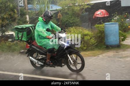 Ratchaburi, Thailand, 14 2022. NOVEMBER, Ein Lieferarbeiter fährt bei Regen mit einem Motorrad auf der Straße der Stadt Stockfoto