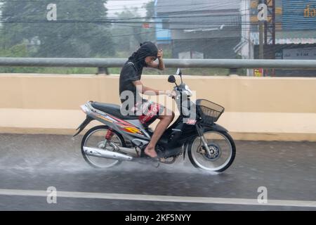 Ratchaburi, Thailand, 14 2022. NOVEMBER, Ein junger Mann fährt auf einem Motorrad und schützt seine Augen vor dem starken Regen mit seiner Hand Stockfoto