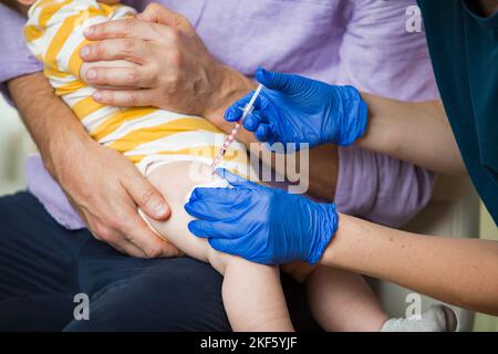 Krankenschwester mit chirurgischer Maske und in Handschuhen, die einem Säugling in der Klinik eine Impfstoffinjektion verabreicht. Säuglingsimpfung. Stockfoto