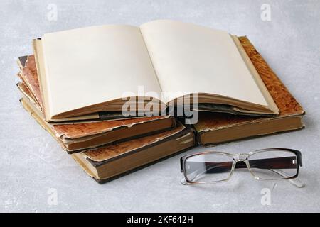 Ein offenes Vintage-Buch oder ein Notizbuch in einer Staubjacke auf einem Stapel alter, schäbiger Bücher und Lesebrillen Stockfoto