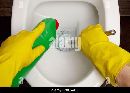 Toilettenreinigung und Desinfektion. Reiniger in gelben Gummihandschuhen reinigt die Toilettenschüssel mit einer Bürste und einem Desinfektionsmittel Stockfoto