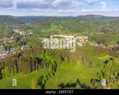 Desna V Jizerskych horach Stadt in der Mitte der grünen Hügel des Isergebirges an sonnigen Sommertag. Tschechische Republik. Luftaufnahme von der Drohne. Stockfoto