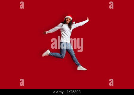 Emotionale hübsche schwarze Frau trägt einen Weihnachtsmütze, die über Rot springt Stockfoto