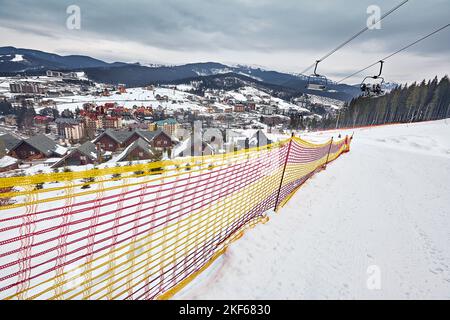 Panorama von Skigebiet, Piste, Menschen auf dem Skilift, Skifahrer auf der Piste zwischen grünen Pinien und Schneelanzen. Stockfoto