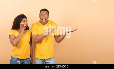 Omm, überprüfen Sie dies. Überglücklich schwarzer Mann, der mit dem Finger auf den Kopierplatz auf offener Handfläche zeigt, Peach-Studio-Hintergrund, Panorama Stockfoto