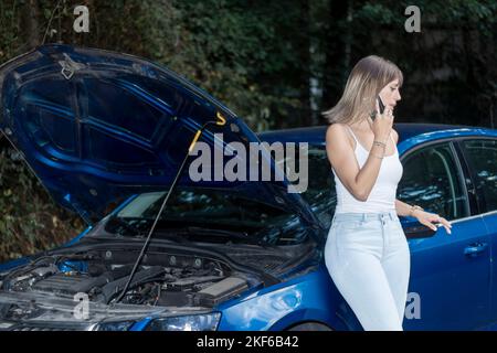 Verzweifelte junge Frau ruft Nothilfe in der Nähe eines kaputten Autos auf der Straße. Hilfe ist erforderlich. Autoservice. Stockfoto