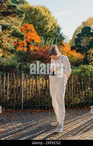 Schöne junge Frau macht Fotos mit einer professionellen Kamera im Herbstwald. Lächelndes Mädchen genießen Herbstwetter. Ruhe, Entspannung, Lifestyle Stockfoto