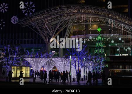 Ein überfüllter Weihnachtsmarkt und festliche Beleuchtung vor dem Bahnhof Hakata in Fukuoka, Japan. Ein später Novemberabend. Stockfoto