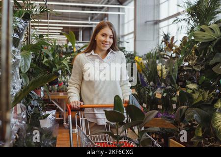 Schöne Erwachsene Frau mit Wagen wählt Topfpflanzen in einem Gewächshaus oder Gartencenter Stockfoto