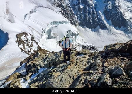 Beschreibung: Bergsteiger klettert auf einer Felsküste mit Panoramablick auf die Tiefen des Rottals im Hintergrund. Jungfrau-Höhenweg, Berner Alpen, Stockfoto