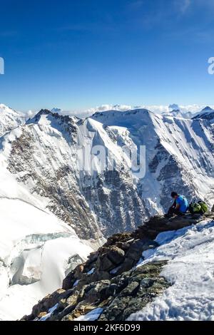 Beschreibung: Bergsteiger zieht Steigeisen an mit Panoramablick auf die Tiefen des Rottal im Hintergrund. Jungfrau-Höhenweg, Berner Alpen Stockfoto