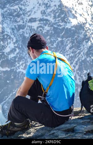 Beschreibung: Bergsteiger zieht Steigeisen an mit Panoramablick auf die Tiefen des Rottal im Hintergrund. Jungfrau-Höhenweg, Berner Alpen Stockfoto