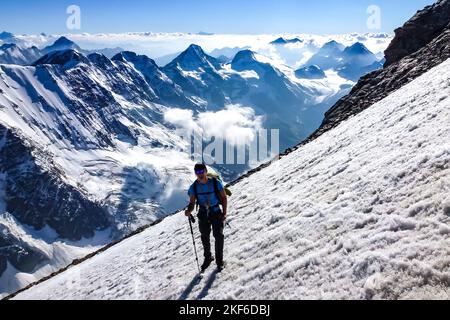 Beschreibung: Bergsteiger mit Steigeisen und Eispickel wandern auf steilem Schneefeld auf der Jungfrau mit Panorama-Berglandschaft im Hintergrund. Jungfrau Stockfoto