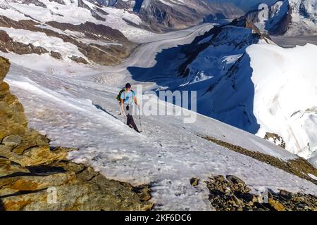 Beschreibung: Bergsteiger mit Steigeisen und Eispickel klettert felsiges Gelände auf der Jungfrau mit Aletschgletscher im Hintergrund. Jungfrau-Höhenweg, Berner A Stockfoto