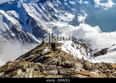 Beschreibung: Begeisterter Bergsteiger beim Wandern auf dem Jungfraugipfel mit Panoramablick auf die Berge im Hintergrund. Jungfrau-Höhenweg, Berner Alpen, Schweiz Stockfoto