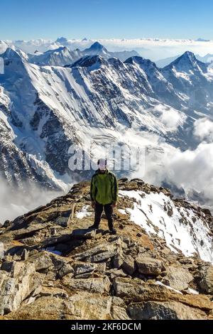 Beschreibung: Begeisterter Bergsteiger beim Wandern auf dem Jungfraugipfel mit Panoramablick auf die Berge im Hintergrund. Jungfrau-Höhenweg, Berner Alpen, Schweiz Stockfoto