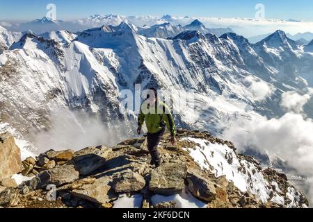 Beschreibung: Begeisterter Bergsteiger beim Wandern auf dem Jungfraugipfel mit Panoramablick auf die Berge im Hintergrund. Jungfrau-Höhenweg, Berner Alpen, Schweiz Stockfoto