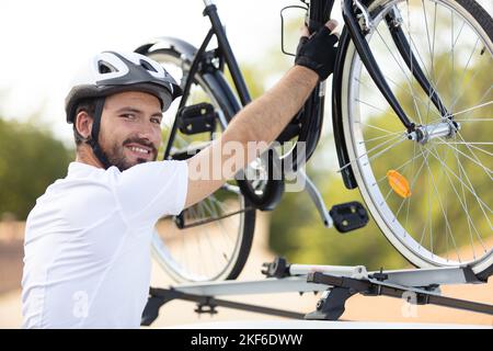 Der junge Mann installiert sein Fahrrad auf dem Autodach Stockfoto