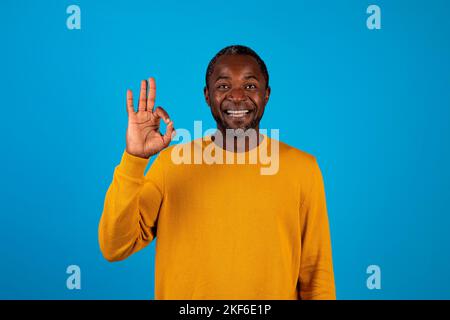 Fröhlicher schwarzer Mann, der eine Geste in Ordnung zeigt, isoliert auf Blau Stockfoto