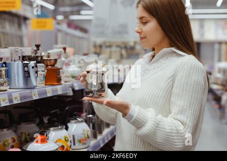 Junge Frau, die Kaffee aus Stahl in der Abteilung für Utensil-Gerichte im Supermarkt wählt Stockfoto