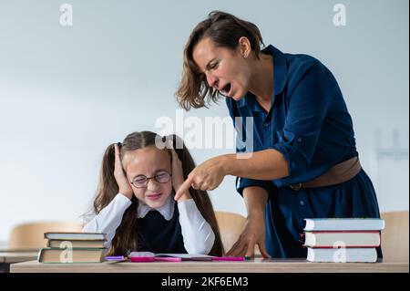 Eine Lehrerin schreit eine Schülerin an. Das kleine Mädchen bedeckt ihre Ohren mit den Händen. Stockfoto