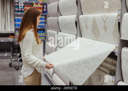 Junge Frau wählen Tapete im Baumarkt. Home Design und Renovierungskonzept Stockfoto