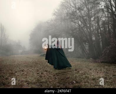 Eine junge Frau im Nebel trägt einen grünen Mantel und hält einen brennenden Laternenlappen Stockfoto